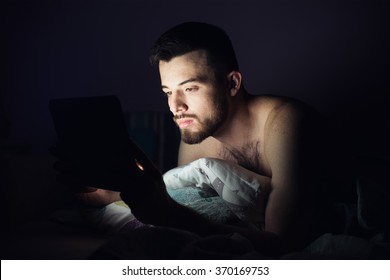 Man  is working at night, lying on the sofa in the living room with tablet. student looks tablet pc late at night before sleep in the room - Powered by Shutterstock