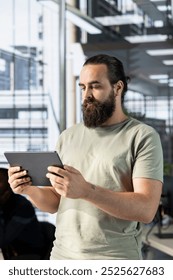 Man working in office developing software in Java programming language using device. Programmer walking through workspace with tablet, thinking how to solve coding problems