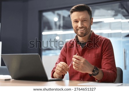 Man Working in Office Setting Using Laptop and Smiling During the Day