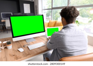 Man working on desktop computer and laptop with green screens in a modern office setting