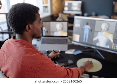 Man working on detailed 3D animation project at modern office desk, engrossed in development on dual monitors with laptop and other tools surrounding - Powered by Shutterstock