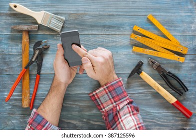 Man Working On A DIY Project With His Phone, Wood Shavings And Carpentry Tools And Construction All Around, Top View