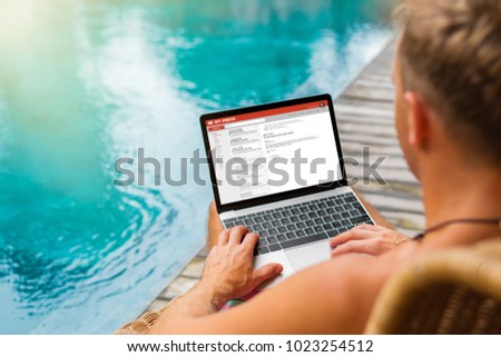 Man working on laptop by the pool while on vacation