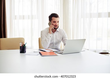 Man Working On The Laptop And Calling Someone On The Phone In The Modern White Office