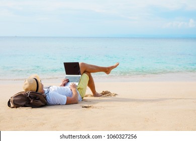 Man working on laptop computer while relaxing on the beach
