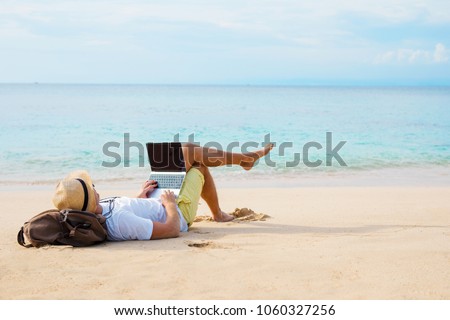 Man working on laptop computer while relaxing on the beach