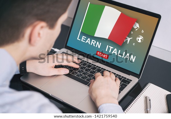 Man working on\
laptop with LEARN ITALIAN on a screen. Education learning italian\
language school concept\
