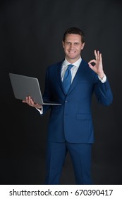 Man Working On Laptop And Making Ok Gesture On Black Background. Happy Businessman Or Manager Smiling In Blue Formal Suit. Technology For Business. Fashion And Dress Code. Blogging And Weblog