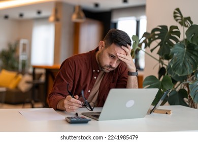 Man working on laptop while sitting at his working place in his apartment. Tired brown haired man taking glasses off working too long at computer. Exhausted male suffer from headache. - Shutterstock ID 2241985479