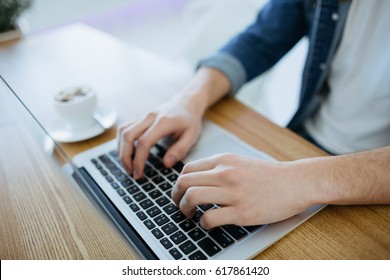 Man working on a macbook or laptop in cafe. Young freelancer is sitting in cafe and typing or searching some information on laptop. Side view