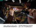 Man working on network server, holding flashlight and connecting cables inside server rack, focusing on maintenance and troubleshooting in data center environment