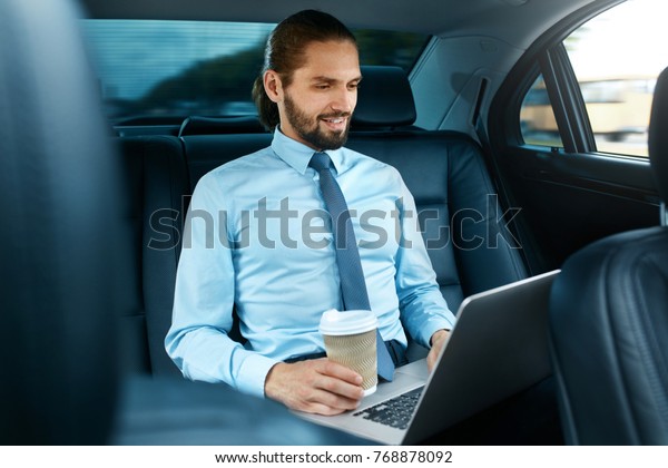 Man\
Working On Notebook And Drinking Coffee in Car. Attractive\
Successful Businessman in Formal Wear Going To Work With Laptop And\
Hot Drink In Car. Business Travel. High\
Resolution.