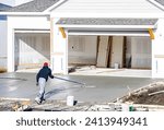 Man working on smoothing concrete driveway for the new home build at construction site. Architecture and exterior structure base progress, safety foundation pavement ground. Real estate industry.