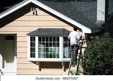 Man Working Outdoor On Ladder Painting The House