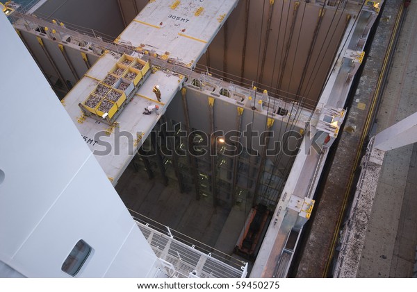 man working over\
precipice (cargo hold)aboard container ship during cargo operation\
in port terminal