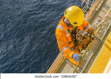 Man working overboard. Abseiler complete with personal protective equipment (PPE) climbing and hanging at the edge of oil and gas rig platform in the middle of sea.
