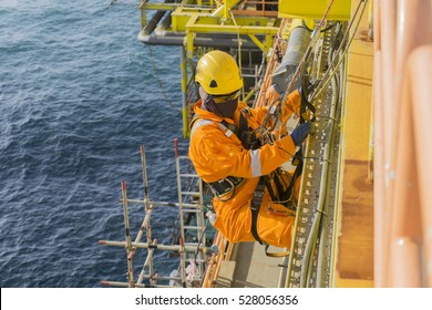 Man Working Overboard. Abseiler Complete With Personal Protective Equipment (PPE) Climbing And Hanging At The Edge Of Oil And Gas Rig Platform In The Middle Of Sea.