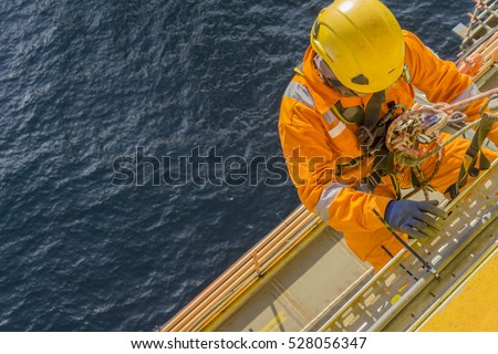 Man working overboard. Abseiler complete with personal protective equipment (PPE) climbing and hanging at the edge of oil and gas rig platform in the middle of sea.