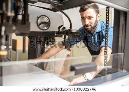 Man working with paper sheets feeling into the printing machine at the manufacturing
