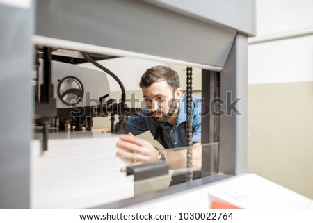 Man working with paper sheets feeling into the printing machine at the manufacturing