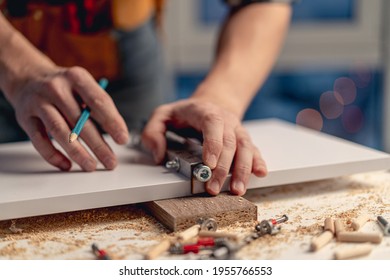 Man working with pencil marking holes during process of wooden furniture manufacturing in workshop
