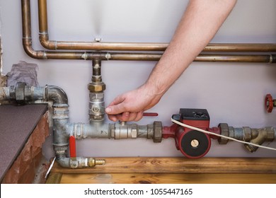 Man working at pipes. Employee's hand turning on or turning off water supply in the boiler room. Commercial plumbing company. Professional service concept. 