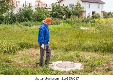 Man Working Plumber With A Tire Iron At A Sewer Well In The Countryside. Maintenance Of Septic Tanks And Water Wells.