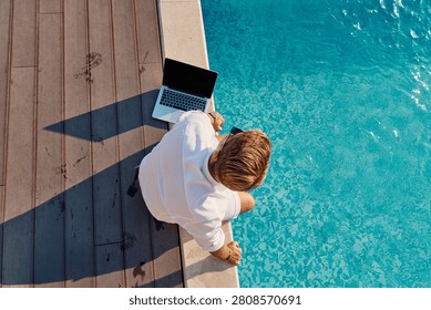 Man Working Remotely By a Pool With Laptop on Deck During Sunny Summer Morning