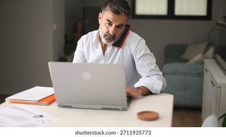 Man working remotely from home, using laptop and talking on phone, balancing work life demanding a multitasking approach
