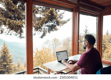 Man working remotely with laptop overlooking a scenic mountain view - Powered by Shutterstock