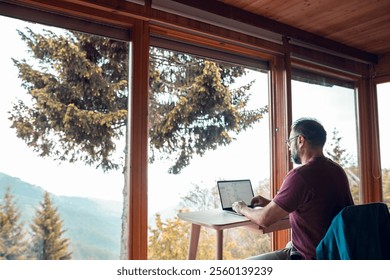 Man working remotely on laptop from mountain cabin - Powered by Shutterstock