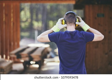 Man Working In Sawmill. Rear View Of The Worker With Headset. 