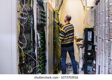 Man is working in the server room of the data center. The engineer connects the wires to provide Internet communication. The system administrator is  next to the rack with computer equipment.