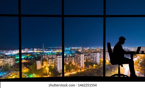 The Man Working At The Table Near A Window With A Night City View