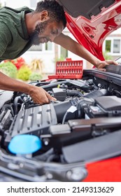Man Working Under Hood Of Car Fixing Engine With Wrench