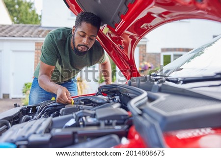 Man Working Under Hood Checking Car Engine Oil Level On Dipstick