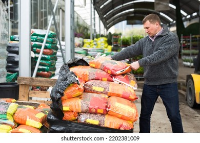 Man Working In Warehouse At Garden Store, Stacking Bags With Drainage And Substrate For Houseplants On Pallets