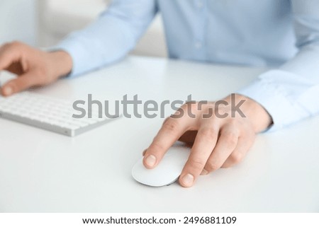 Man working with wireless mouse and computer keyboard at white table indoors, closeup
