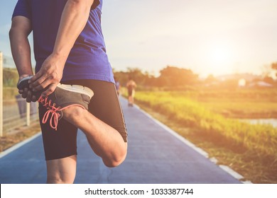 Man workout and wellness concept : The asian runner warm up his body before start running on road in the park. Shot in morning time, sunlight and warm effect with copy space for text or design
