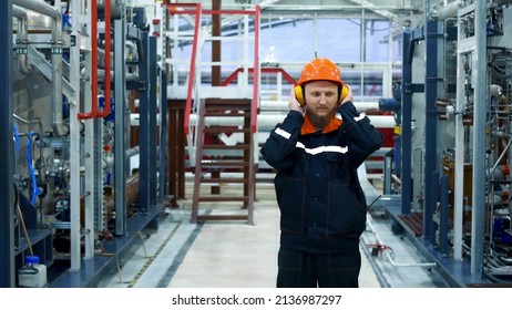 The Man In The Workplace. A Bearded Man In A Helmet Puts On Headphones In The Gas Compression Shop. Noisy Work Space. Oil And Gas Industry