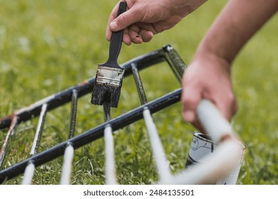 The man works with a brush and applies black paint to the rust. A worker paints metal structures in close-up. Rust removal. Half of the painted surface. Smearing with a brush. - Powered by Shutterstock