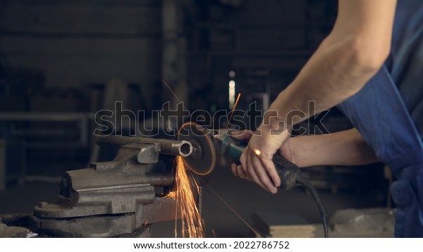 man works with a circular saw. Sparks fly from the
hot metal. man was working hard on steel. Close-up, slow motion in
garage. An angle grinder cuts an iron billet clamped in a
locksmith's vise.