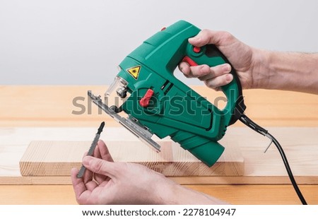 A man works with an electric jigsaw for wood on a wooden table with and without gloves and measures with a tape measure