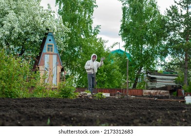 A man works in the garden, against the backdrop of an original colorful wooden garden toilet in the village, on a plot with tall green trees. garden exterior. Russian street toilet.