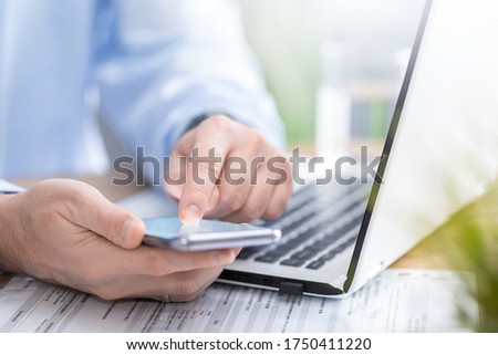 The man works at home and uses a smart phone and a notebook laptop computer. Silhouette of a busy man. He holds and using phone.
