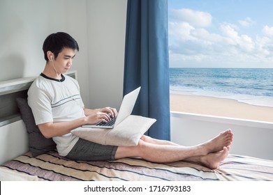 Man Works From Home Using Laptop In Bedroom With Beach View Through The Window