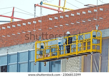 A man works on the facade of a building with suspended scaffolding