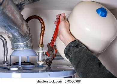 Man Works On A Hot Water Heater With A Pipe Wrench