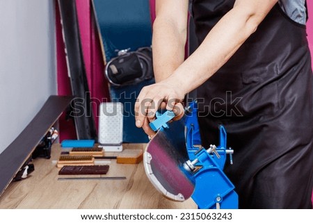 Man in a workshop hold skis on vises, use sharpen tool for sharpening ski edges