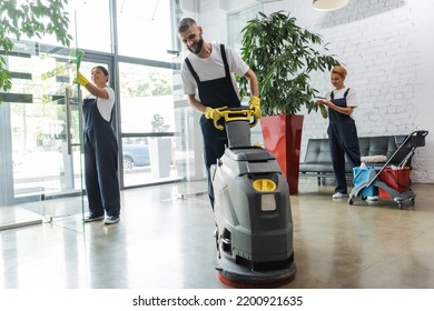 man in workwear with floor scrubber machine near interracial women cleaning office lobby - Shutterstock ID 2200921635